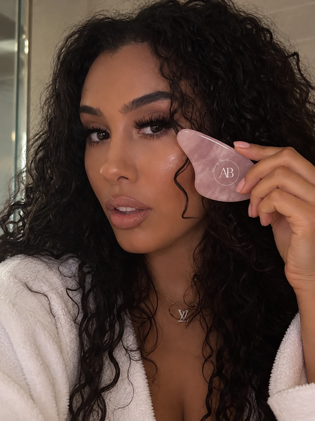 Woman holding the Alluring Beauté rose quartz gua sha against her cheekbone